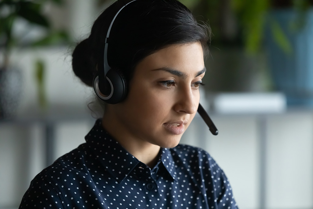 A woman wearing modern wireless headset with microphone consulting on a video call