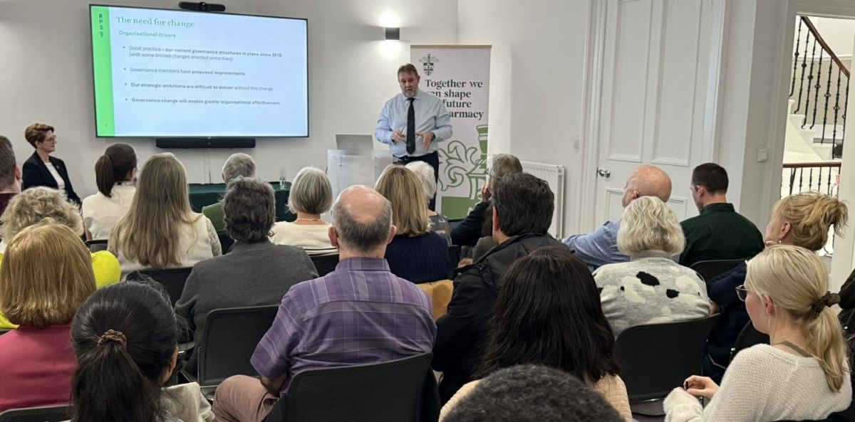 Paul Bennett stood in front of screen with powerpoint presentation presenting to group of people in a room