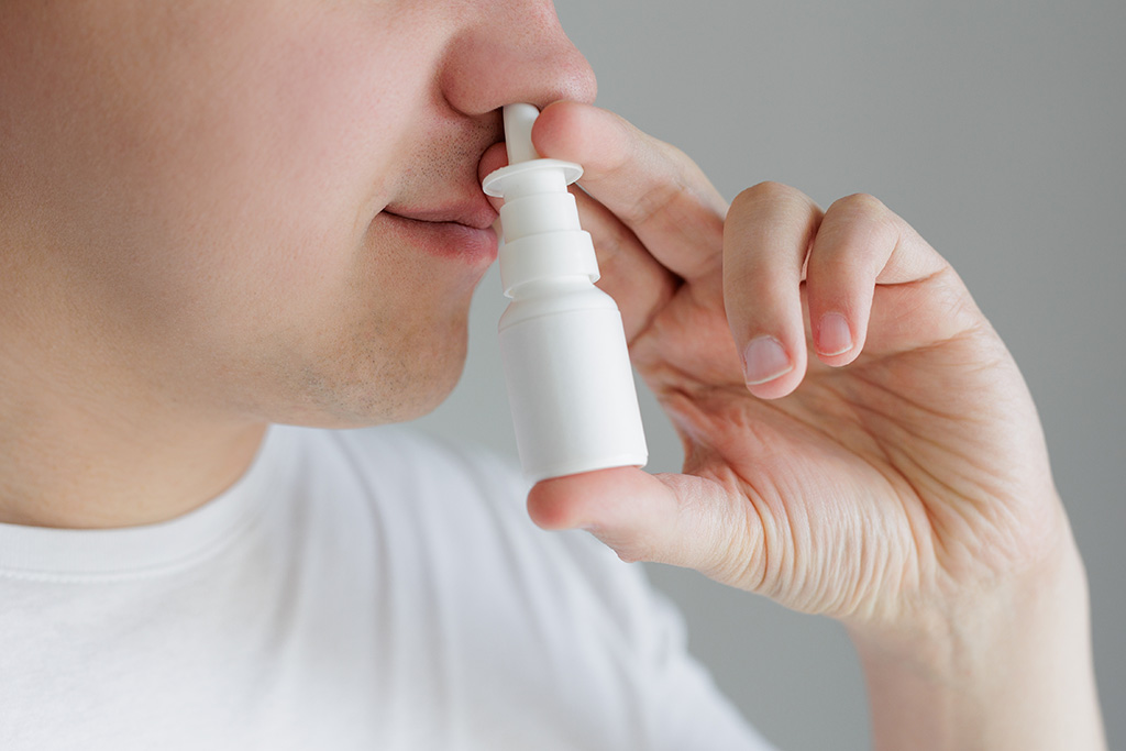 Closeup of young man in white tshirt spraying drops in nose