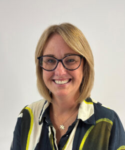Laura smiles in front of a grey background, wearing glasses and a coloured shirt