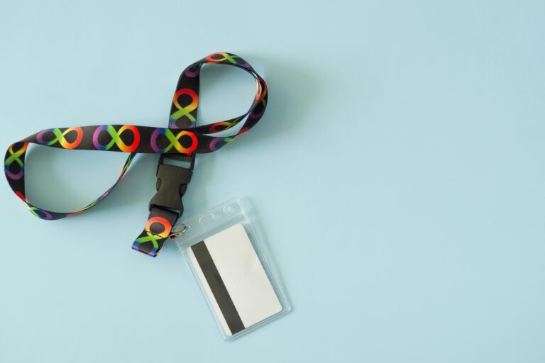Top view to black neck strap lanyard with rainbow colors infinity symbols and card holder on light blue background. Infinity is symbol of autism disorder, ADHD, neurodiversity.