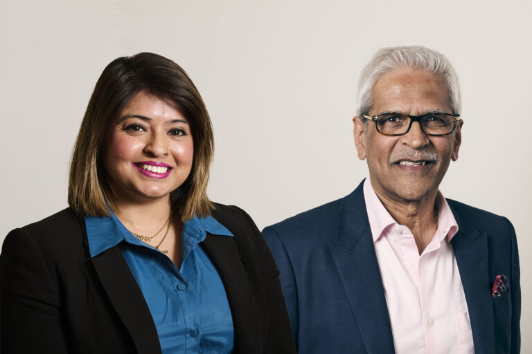 Amandeep on left wearing blue shirt and blazer, Mahendra on right with pink shirt and blazer, both in front of grey background