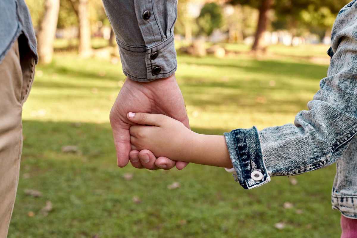 Child and parent holding hands in nature setting.