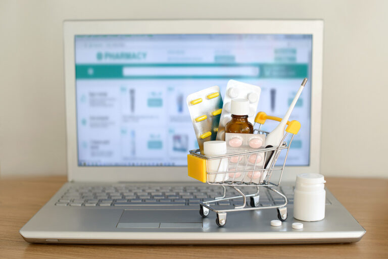 Shopping cart with medications in front of laptop with pharmacy website on screen