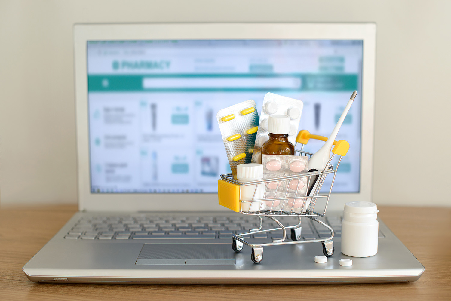 Shopping cart with medications in front of laptop with pharmacy website on screen