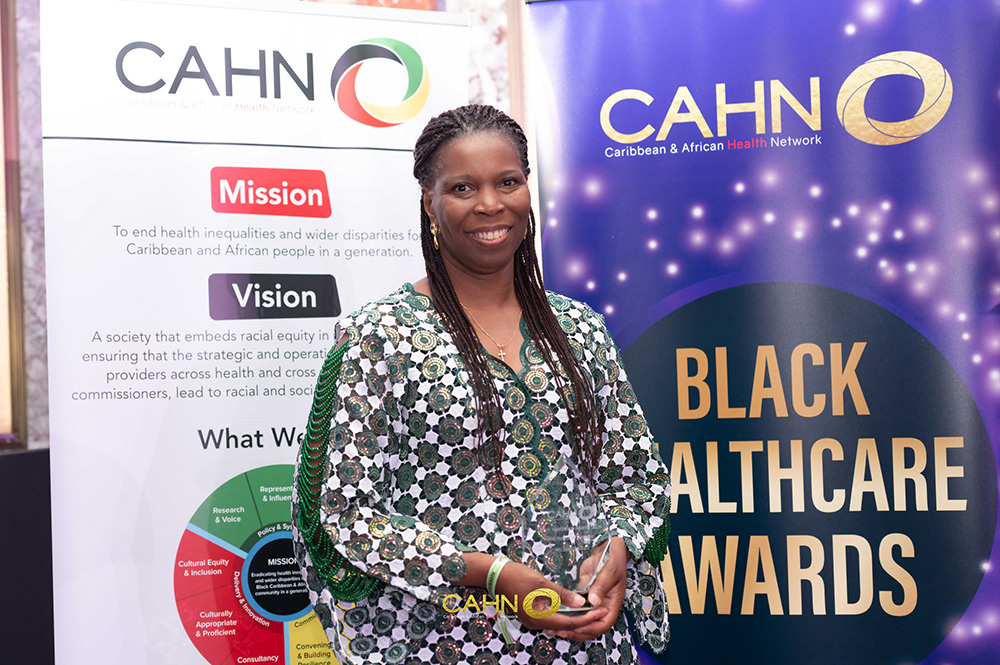 President, Tase Oputu, being named Pharmacist of the Year at the Black Healthcare Awards. Tase smiles in front of two banners, white and purple