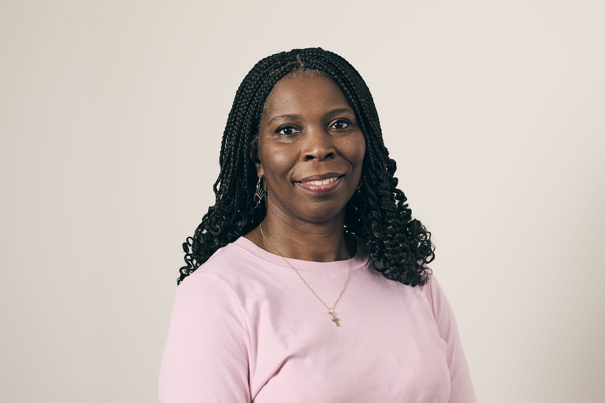 Tase looks serious wearing a pink top, hair down in front of a neutral background