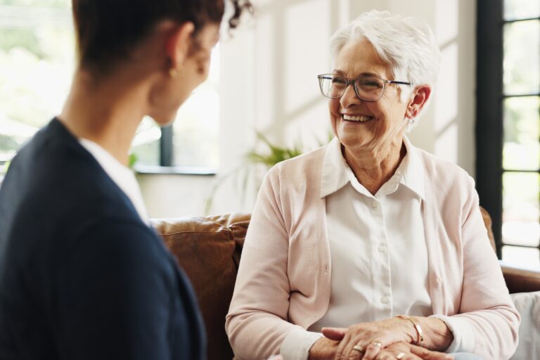 A volunteer and a senior woman in living room for rehabilitation talking and smiling