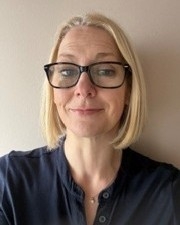 Head and shoulders image of Claire Chapman, member of the ‘Pharmacy: Delivering a Healthier Wales’ delivery board, wearing a dark shirt and black rimmed glasses