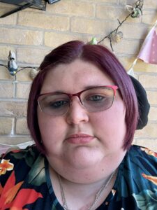 Head and shoulders image of Katie-Rose Stone, BA (Hons) Health and Social Care, wearing a floral top in front of a brick wall