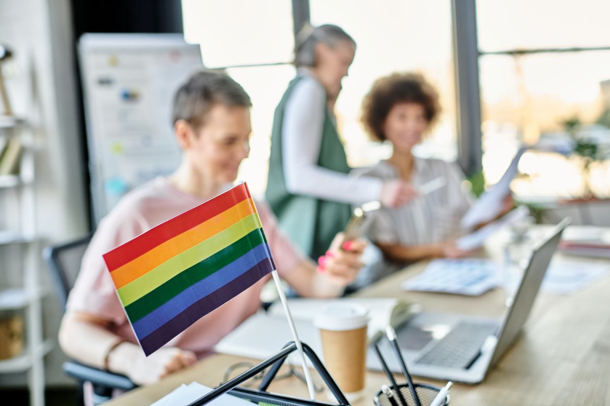 Focus on rainbow flag displayed on office table in front of blurred diverse businesswomen.
