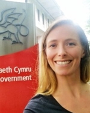 Head and shoulders image of Natalie Proctor, member of the ‘Pharmacy: Delivering a Healthier Wales’ delivery board, wearing a black top in front of a red banner