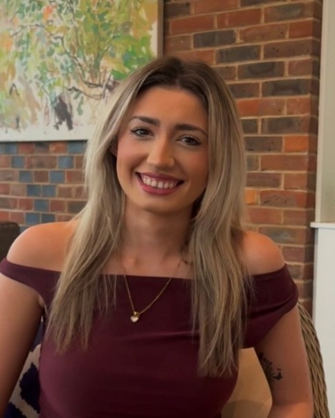Head and shoulders image of Kayleigh Williams, member of the ‘Pharmacy: Delivering a Healthier Wales’ delivery board, wearing a dark red top in front of a brick background