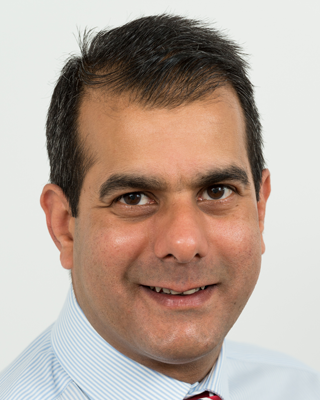Head and shoulders image of Sudhir Sehrawat, member of the ‘Pharmacy: Delivering a Healthier Wales’ delivery board, wearing a blue striped shirt