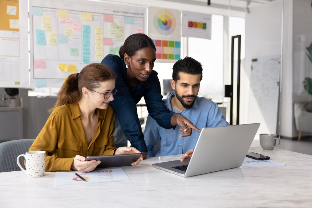 Three colleagues working together around a laptop and tablet in an office.