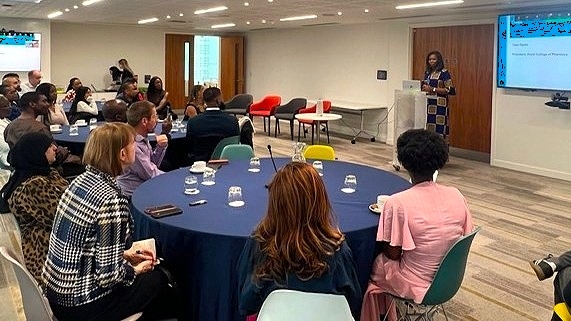 Tase Oputu addressing a room of people sitting at tables from a lectern,