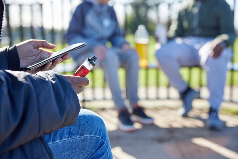 Close-up of young people vaping and drinking alcohol in a park.